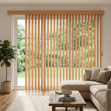 Load image into Gallery viewer, Wood Grain Faux Wood PVC Vertical Blinds expertly filter natural light, complementing beige tones and fostering a warm atmosphere in this inviting open-concept living space.