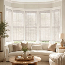 Load image into Gallery viewer, Transform your space with Cordless Woven Wood Shades, perfectly complementing the serene beige atmosphere and natural light filtering through the partially open white blinds.