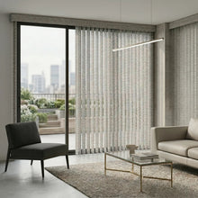 Load image into Gallery viewer, Signature Collection Fabric Vertical Blinds in creamy white beautifully complement gray concrete walls, inviting potted plants and plush furniture amidst a warm and sophisticated atmosphere.