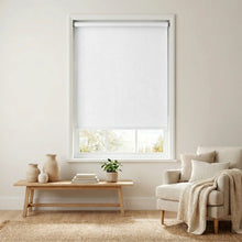 Load image into Gallery viewer, Main view of White Luxe fabric blackout roller shades in a sun-drenched living room featuring minimalist wooden furniture and neutral decor.