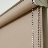 Macro closeup of Beige Economy Basic Vinyl Blackout Roller Shades showcasing the smooth texture and a hanging metal chain.
