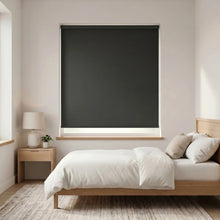Load image into Gallery viewer, Economy Basic Vinyl Blackout Roller Shades in a sleek black hue adorn a serene bedroom, softly blocking out light and creating a cozy ambiance.


