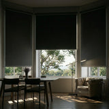 A set of black ProGrade blackout roller shades installed in a bay window dining area to eliminate morning glare.