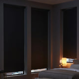 Three black ProGrade blackout roller shades installed on corner windows in a cozy, modern bedroom.