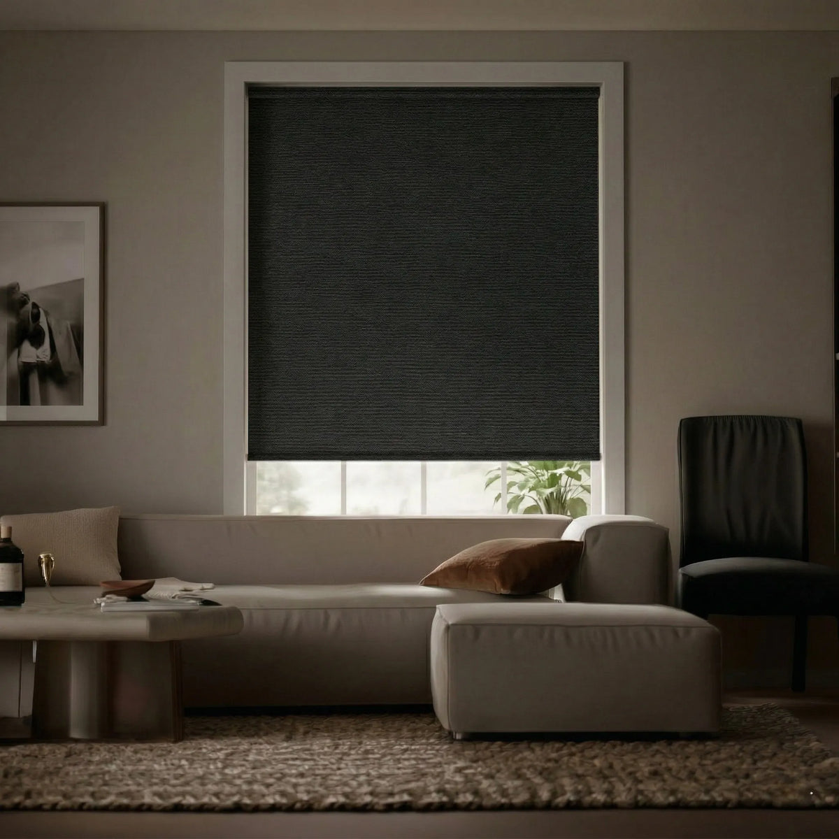 Living room view of an elegant black charcoal signature room darkening roller shade almost, almost fully closed letting in minimal light and giving the room a moody atmosphere