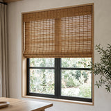 Motorized Woven Wood Shades in warm camel bamboo with a valance, filtering garden light into a dining room with a black-framed window.