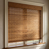 Motorized Woven Wood Shades in warm camel bamboo with a matching valance, the remote control resting on the window sill.