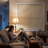 Cream Classic Blackout Vinyl Roller Shade glowing softly behind a woman reading on the sofa at night