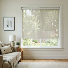 Load image into Gallery viewer, Front-facing view of a cream-colored Natural solar shade with 14 percent openness, providing light filtering and UV protection in a bright sitting area.
