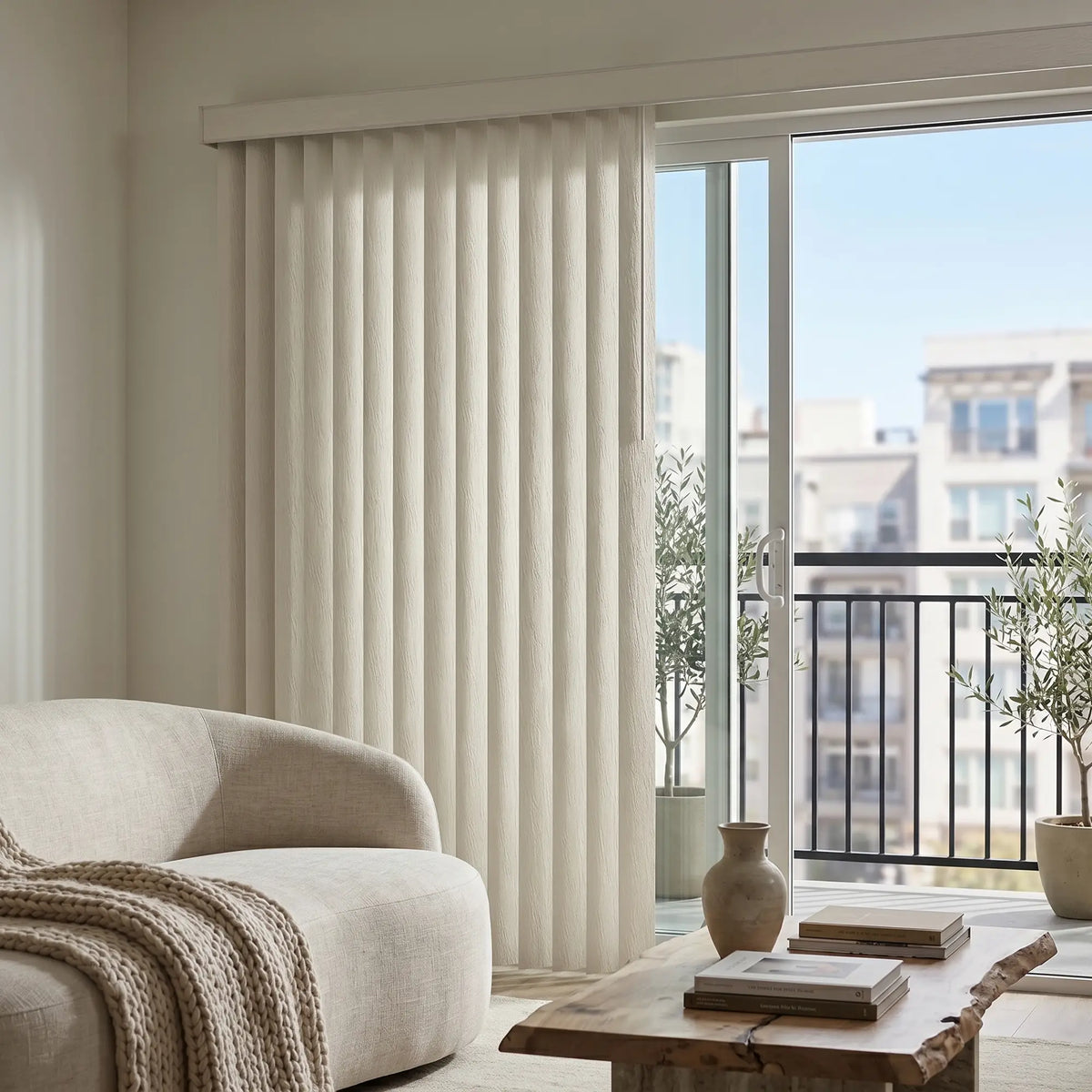 Woodtone Faux Wood PVC Vertical Blinds in creamy white frame softly filtering natural light into this inviting living room with beige couch and balcony access