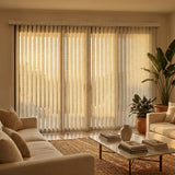 Signature Collection Fabric Vertical Blinds in creamy white perfectly balance natural light and privacy, complementing a beige sofa and lush potted plants in a warm, inviting room.