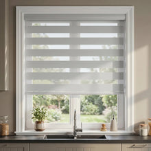Load image into Gallery viewer, Modern kitchen with natural light pours in through white vertical blinds; Zebra Room Darkening Roller Shades complement creamy white hues

