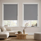 Economy Basic Vinyl Blackout Roller Shades in a modern living room, evoking a cozy atmosphere with gray tones and dimmed light.
