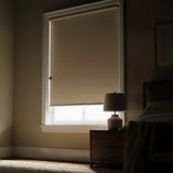 Beige coffee room darkening roller shade in a dim bedroom setting almost closed letting some natural light in thru the bottom