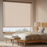 Light tan Flaxen Luxe natural light filtering roller shades in a cozy bedroom with warm wood accents.