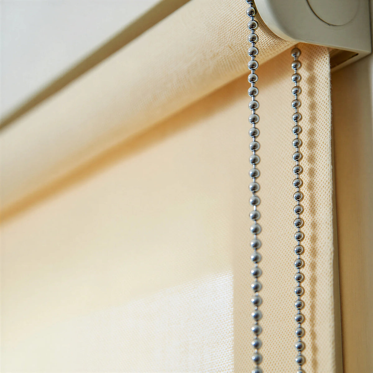 Macro high detail close-up of the Ivory fabric and beaded chain mechanism of a light filtering roller shade.
