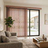 Woodtone Faux Wood PVC Vertical Blinds in Rosy add a touch of whimsy to this neutral-toned living room, where a gray couch and books on a coffee table create a inviting atmosphere.