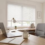 White roller blind shades with a white valance installed on a window in a bright, modern home office setting with a desk, laptop, lamp, and chair.
