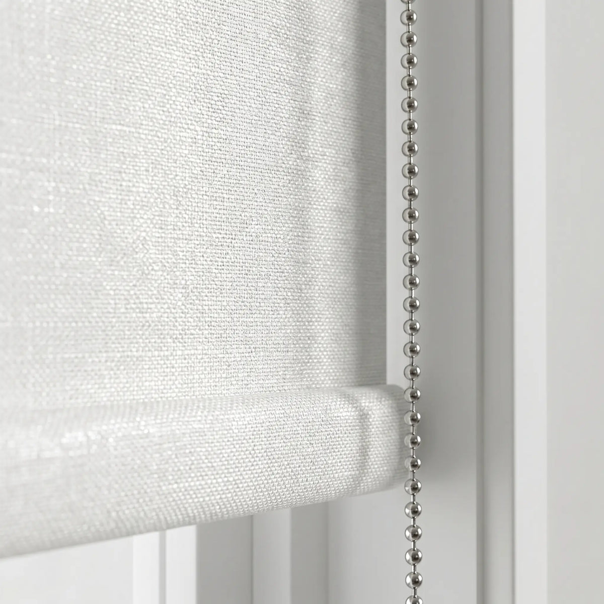 Macro close-up of the textured white Luxe fabric and the durable metallic beaded chain mechanism of the blackout roller shade