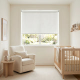 White Luxe fabric blackout roller shades installed in a bright nursery room with a wooden crib and glider, showcasing a light-blocking solution for daytime naps