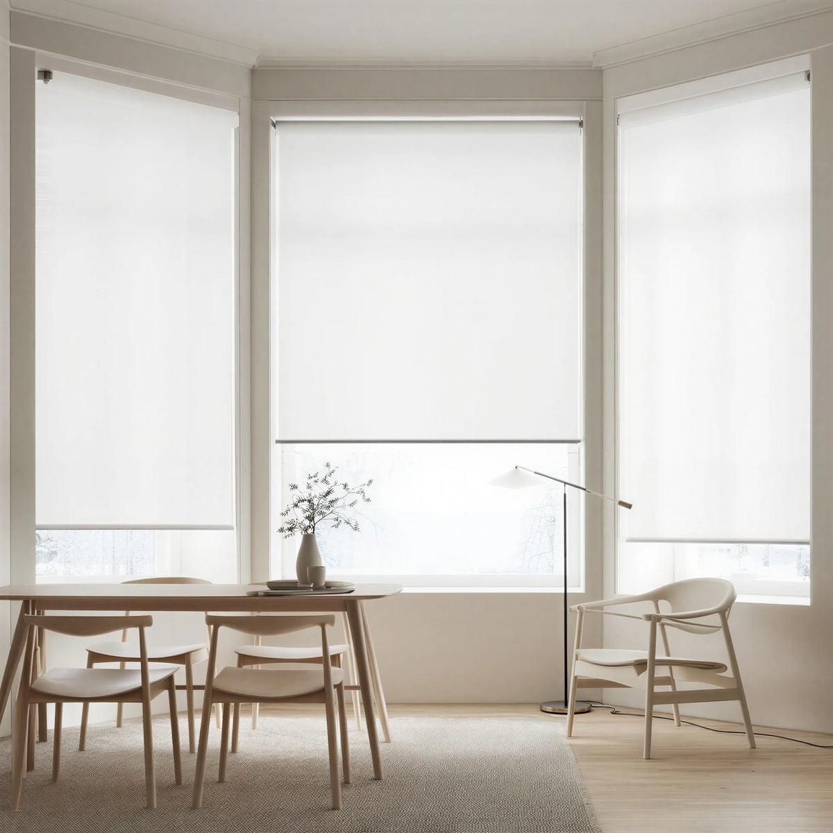 Three white signature light filtering roller shades installed on a large bay window in a modern dining area, showing elegant light diffusing.