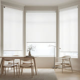 Three white signature light filtering roller shades installed on a large bay window in a modern dining area, showing elegant light diffusing.