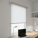 White light filtering roller shades with elegant light diffusing properties installed in a home office setting with a laptop and desk lamp.