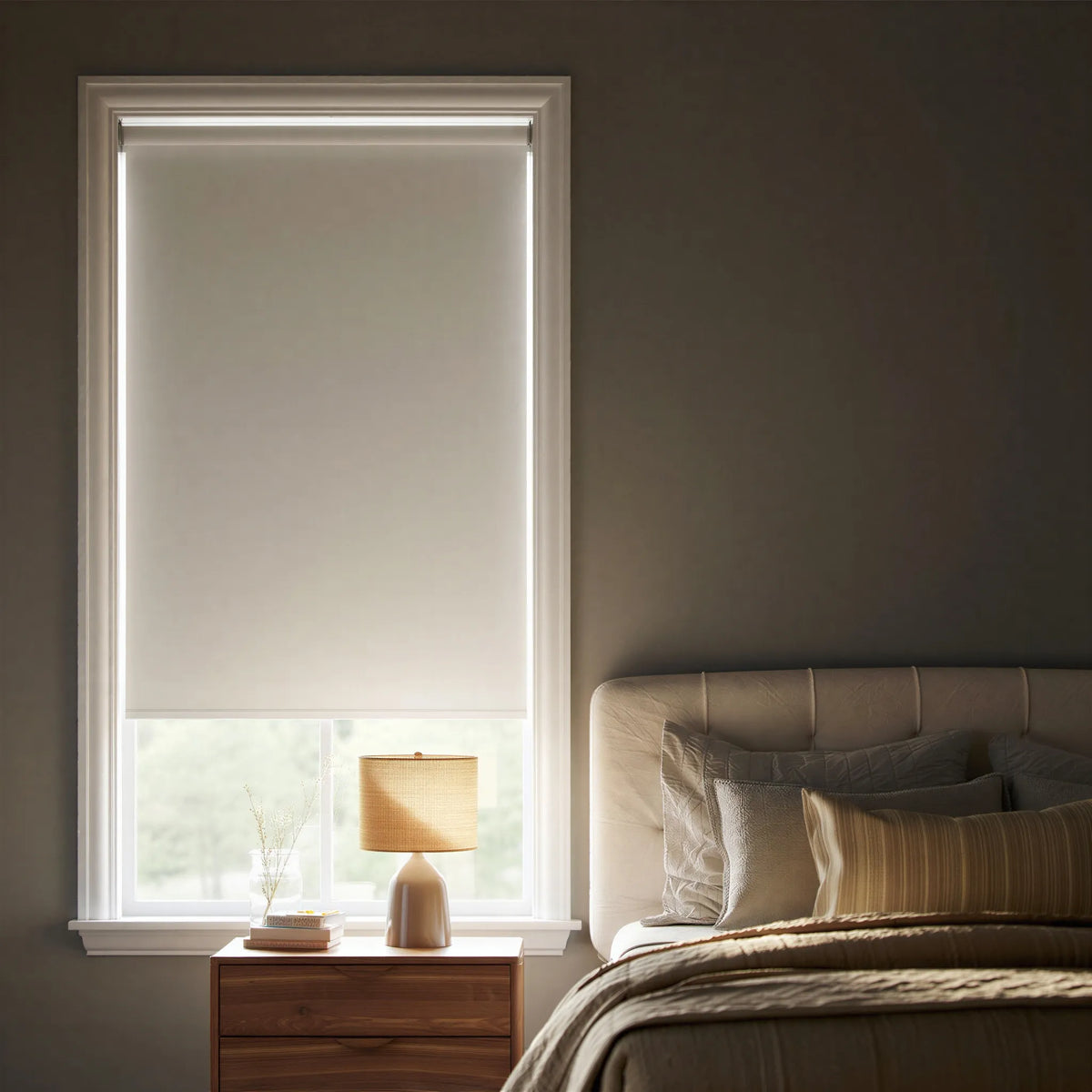 Off-center angled shot of a white elegance room darkening roller shade in a modern bedroom with a bed and pillows visible on the right