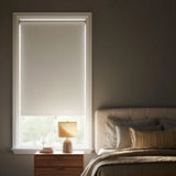 Off-center angled shot of a white elegance room darkening roller shade in a modern bedroom with a bed and pillows visible on the right