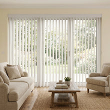 Load image into Gallery viewer, Woodtone Faux Wood PVC Vertical Blinds in crisp white complement this inviting room's warm tones, perfect for a relaxing outdoor retreat.
